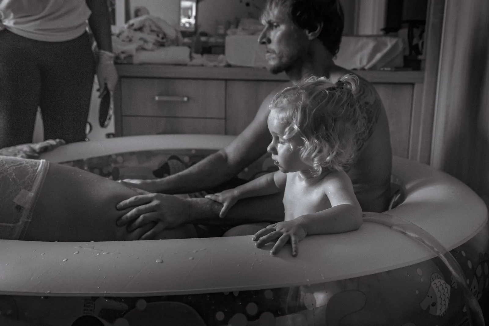 Black and white photograph capturing a supportive family during a home water birth.